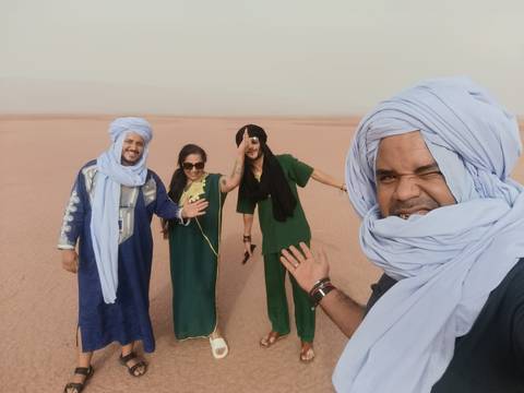       Smiling group selfie in desert wearing colourful traditional outfits and turbans.
  