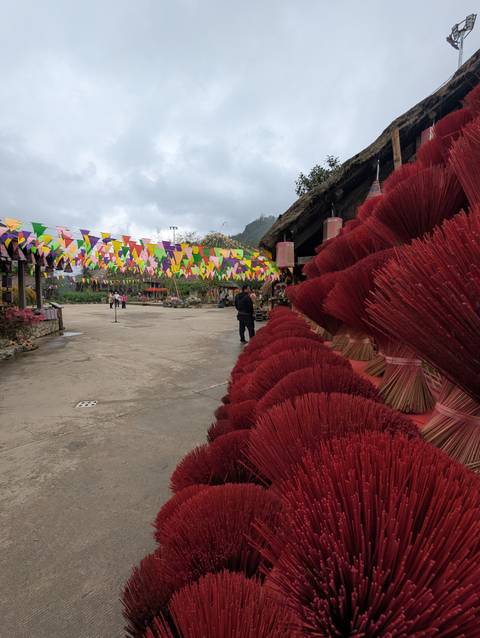       Stacks of vibrant red incense sticks line a village lane decorated with pennant flags
  