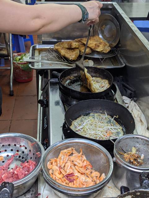       Street-food cook prepares sizzling pancakes in black pans with bean sprouts
  