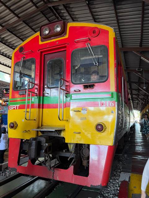       Front of colorful SRT train at station with driver visible through window.
  