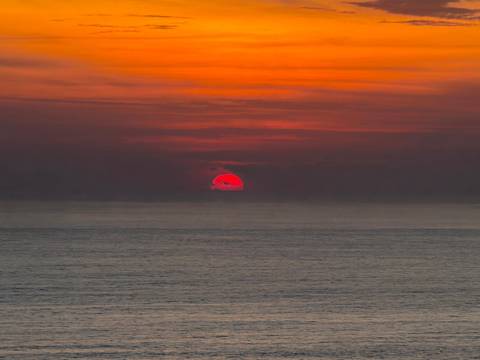       Vibrant red-orange sun setting over calm ocean horizon.
  