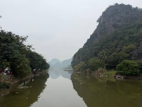       Calm river reflecting karst hills and hazy sky in Ninh Binh.
  