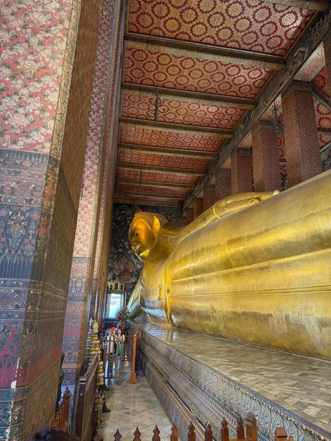       Golden reclining Buddha statue inside an ornately decorated temple hall
  
