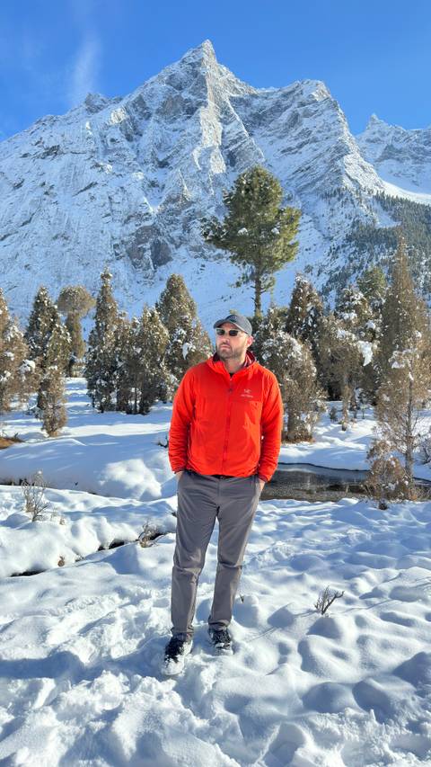       Man in red jacket standing in snowy forested valley with mountains behind
  