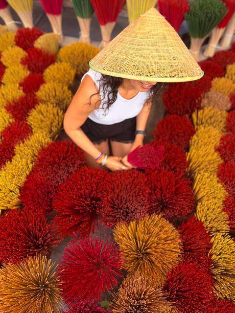       Close-up of woman holding red incense sticks surrounded by vibrant bundles in market
  