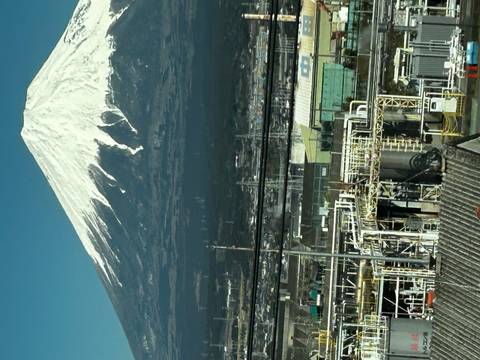       Snow-capped Mount Fuji rises above an industrial foreground under a clear blue sky.
  