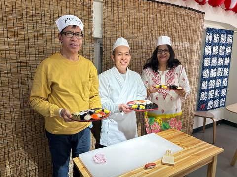       Participants proudly display handmade sushi rolls alongside a Japanese chef in a cooking class.
  