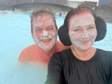       Couple with silica mud masks smile in the milky blue geothermal waters of the Blue Lagoon.
  