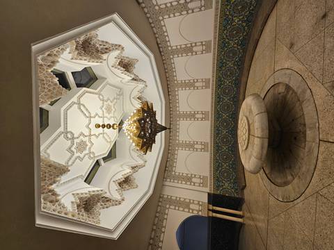       Ornate Moroccan interior with carved stucco ceiling, star motifs, large chandelier and circular stone fountain basin.
  