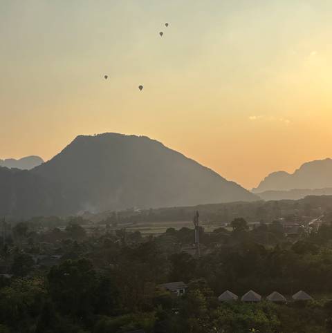       Silhouetted karst mountain and hot-air balloons over hazy valley at sunset.
  