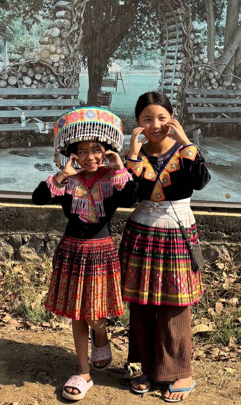       Two girls in colourful hill-tribe attire posing playfully for the camera.
  