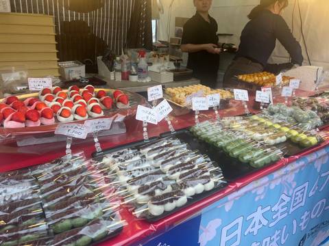       Market stall display of Japanese sweets and skewers neatly arranged with handwritten price tags.
  