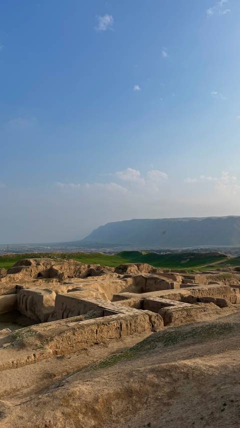       Rolling green hills meet a distant plateau under a hazy afternoon sky.
  