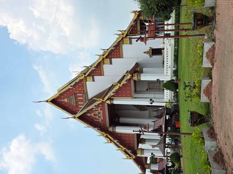      Grand red-white Viharn Phra Mongkol Bophit temple in Ayutthaya with ornate golden gables against a bright sky.
  