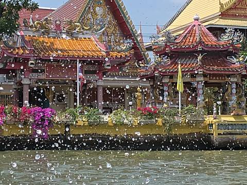       Colorful riverside shrine with ornate roofs seen through sparkling water droplets splashing up from a boat ride
  