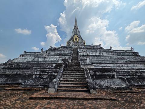       Massive grey-stone pyramid stupa with steep central stairway reaching toward a partly cloudy blue sky
  