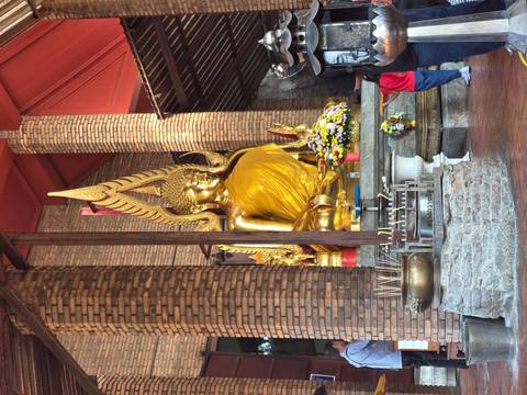       Golden seated Buddha statue draped in saffron inside a brick-walled temple with incense and flowers in front
  
