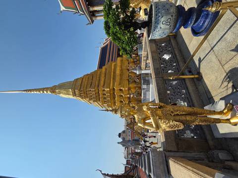       Shimmering golden chedi and guardian statue at Bangkok’s Grand Palace complex bustling with visitors
  