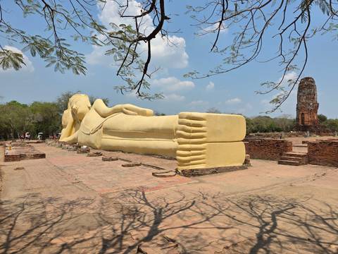       Large outdoor reclining Buddha coated in yellow placed amid ancient brick ruins under blue sky
  