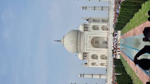       Frontal view of the Taj Mahal with reflecting pool and crowds of visitors lining the pathway
  