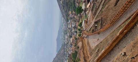       Sweeping hilltop view over ancient ramparts and winding pathways leading to a town nestled in a valley
  