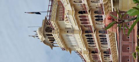       Elegant yellow and red palace building featuring arched windows, balconies and national flag against pale sky
  