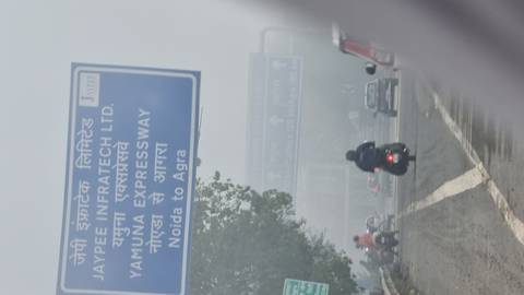       Blurry roadside shot of a blue highway sign indicating Yamuna Expressway to Agra on a foggy morning
  