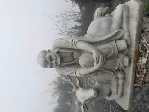       Marble statue of a monk with deer companion shrouded in dense mountain fog
  