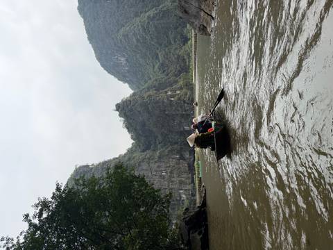      Rowboat navigates muddy river among towering karst cliffs in Ninh Binh, paddled by a local wearing a conical hat
  