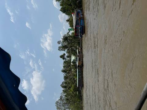       Wide brown river lined by palm trees and simple stilt houses under a bright blue sky in the Mekong Delta
  