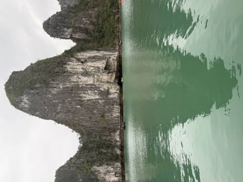       Tall limestone karst rises dramatically from the jade waters of Halong Bay, its reflection mirrored below
  