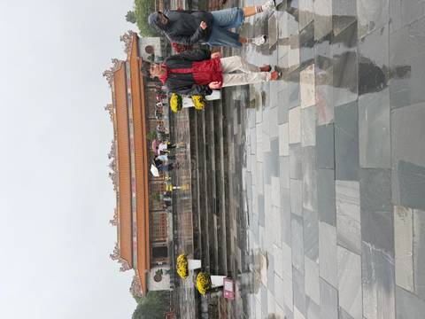      Visitors with umbrellas walk across rain-soaked marble courtyard toward a traditional Vietnamese palace building
  