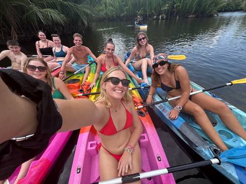       Smiling friends take a selfie while floating on colourful kayaks in clear lagoon water.
  