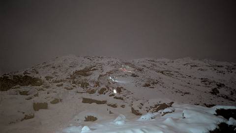       Nighttime scene of snow-covered slope with small lines of climber headlamps ascending in darkness.
  