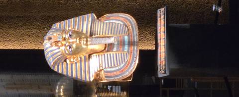       Glittering golden mask of Tutankhamun displayed in a museum case.
  