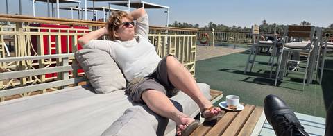       Woman lounges on a sunbed with coffee while cruising the Nile River.
  