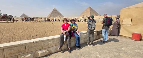       Travelers gather near the pyramids while another visitor photographs them.
  