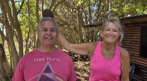       Smiling woman playfully rests a volcanic stone on a man’s head among coastal trees.
  