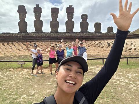       Selfie with smiling guide and group waving in front of moai statues.
  