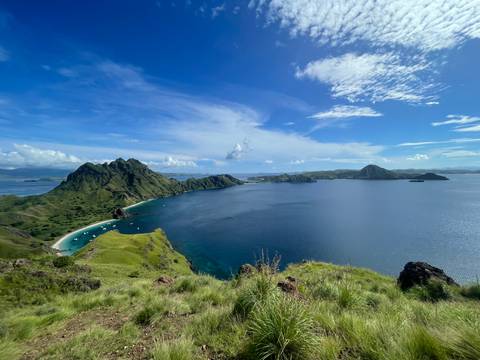       Iconic panoramic view from Padar Island showing turquoise bays, green ridges and deep-blue sea under a bright sky.
  