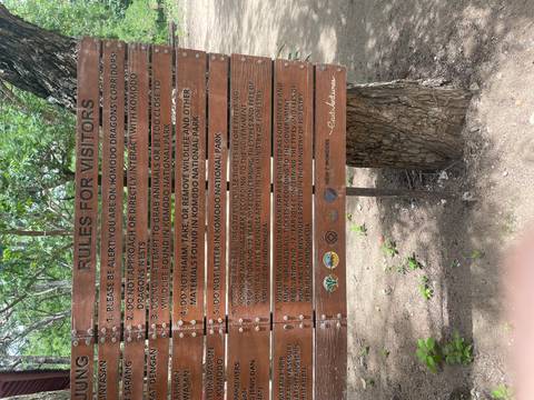       Wooden board listing rules for visitors in Komodo National Park set against trees.
  