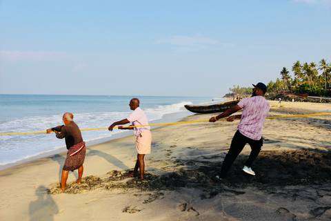      Local fishermen and a traveler haul a long net from the sandy shore into the calm sea.
  