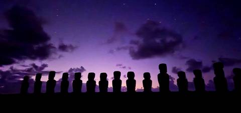       Silhouetted line of moai statues under a starry purple twilight sky on Easter Island.
  