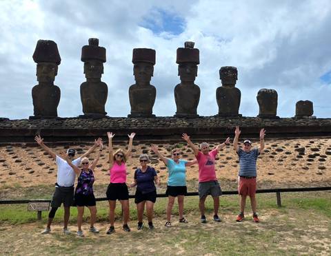       Group of travelers raising arms in front of moai statues on a sunny day.
  