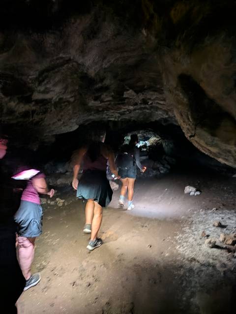       Hikers with flashlights move through a dark lava tube cave.
  