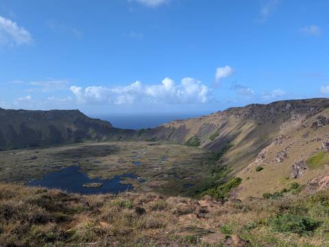       Expansive crater of Rano Kau volcano with marshy blue lake and sea beyond under clear sky.
  
