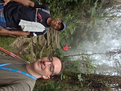       Three hikers pause on a misty jungle staircase, smiling for a selfie during a mountain trek.
  