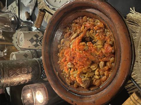       A bubbling Moroccan tagine filled with meat, tomatoes and beans sits on a clay dish at dinner.
  