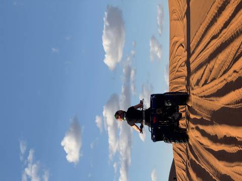       A rider on a blue quad bike carves tracks across golden desert dunes beneath a deep blue sky.
  