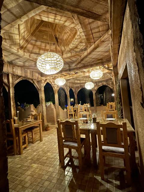       Rustic open-air dining area with wooden arches and hanging lanterns at night.
  